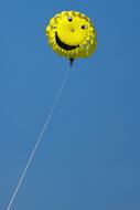 Beautiful, yellow parachute with smile, on the rope, in the blue sky in summer