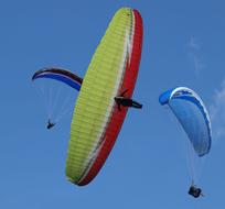 People, doing paragliding with the colorful parachutes, in the blue sky with clouds