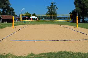 Beautiful sand field for volleyball with yellow web, among the green grass and trees