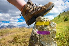 Person's leg in hiking shoe on the rock with yellow and purple markup, on the beautiful and colorful mountain