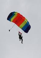 Person, doing skydiving on the colorful parachute, under the cloudy sky