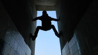 Silhouette of a boy, climbing on the walls, at blue sky on background