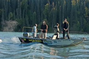 Fishermen fishing on the boat on the river, near the green trees on the shore in Alaska