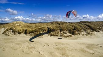 Person doing paragliding above the beautiful and colorful dune of the North Sea, under the blue sky with clouds