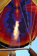 Colorful hot air balloon with shapes, flame and ropes, under the blue sky