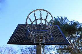 Close-up of the metal basketball hoop at the court, among the trees, under the blue sky