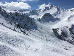 Ski track on the beautiful, snowy mountain in sunlight, under the blue sky with white clouds