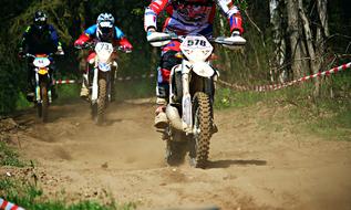 Motocross riders, riding on sand among the plants