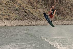 Guy doing wake boarding on the water, near the shore