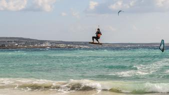 Person doing kite surfing in the colorful water with waves, on the beach