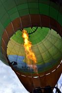 Flying, colorful hot air balloon with flame, under the blue sky with white clouds