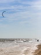 Kite surfer on the beautiful sandy beach with waves, under the blue sky with clouds