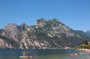 People on the beach of the beautiful Garda Lake among the mountains with green plants, in Italy, under the blue sky