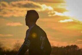Football player in uniform, among the plants, at colorful and beautiful sunset