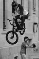 Black and white photo of the rider doing BMX trick near the photographer and building