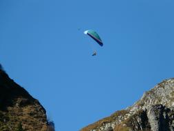 Paraglider Flying in clear sky over rocks