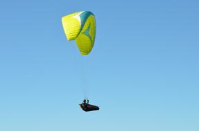 Person on the colorful hang glider in sunlight, under the blue sky