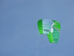 Close-up of the green, white and black parachute of the flying person, under the blue sky