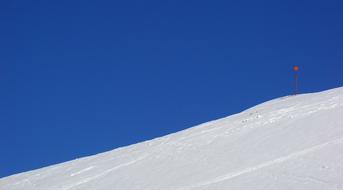 Beautiful, snowy mountain with skiing traces and pole, in the winter, under the blue sky