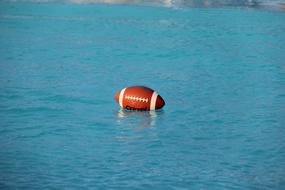 Close-up of the orange, black and white rugby ball swimming in the water with ripple