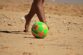 Man near the colorful, shiny soccer ball on the sandy beach in sunlight