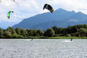 People doing kitesurfing with colorful parachutes, on the water, near the beautiful mountains with green plants