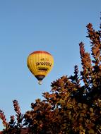 Flying, colorful hot air balloon, above the colorful trees, under the blue sky