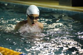 Swimmer girl in swimming hat and goggles, swimming in water with ripple