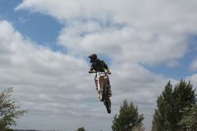 Moto cross rider in helmet, in the jump, among the colorful trees, under the blue sky with clouds