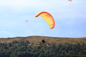 People doing paragliding with colorful parachutes, above the beautiful and colorful hills with plants, under the blue sky with white clouds