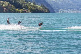 People doing water sports in the water with waves, near the beautiful mountains with green plants