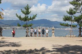 Girls on bikes, on the sandy beach with green trees, at background with the mountains