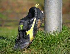 Close-up of the dirty football shoe, near the pole, among the green grass