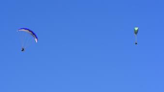 Couple paragliding with colorful parachutes, in the blue sky