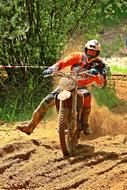 Motorcycle rider in colorful helmet, on the dirty road in sunlight, among the green plants