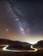 Beautiful landscape of the road with colorful lights in movement on the hills, at colorful sky, at night