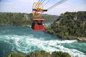 Red and yellow cable car, above the beautiful Niagara Falls, among the green trees in New York, United States