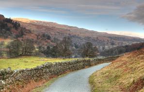 Road fenced with aged stone wall, scenic rural Landscape