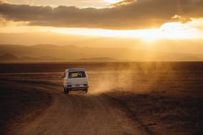 Volkswagen car driving away on dirt road at colorful sunset