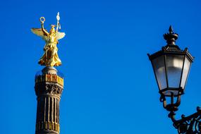 photo of a wrought-iron street lamp against the background of a golden sculpture in Berlin