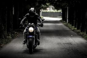 Black and white photo with the biker in helmet, on the motorcycle in movement, on the road