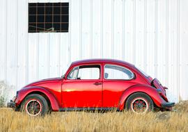 red retro car beetle parked by the barn