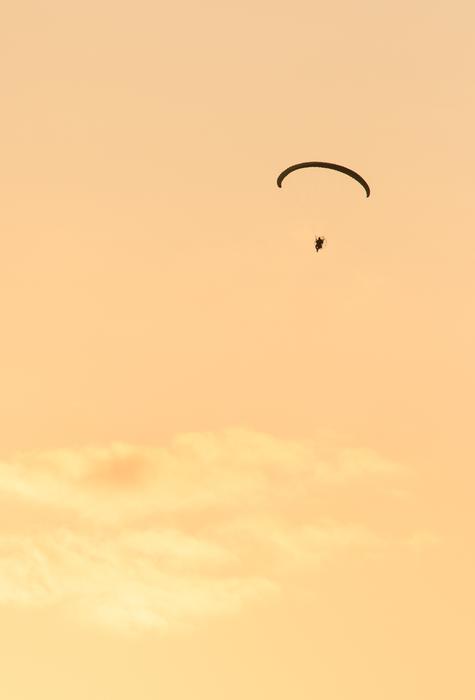 Person, flying on the parachute, at beautiful and colorful twilight, with the clouds