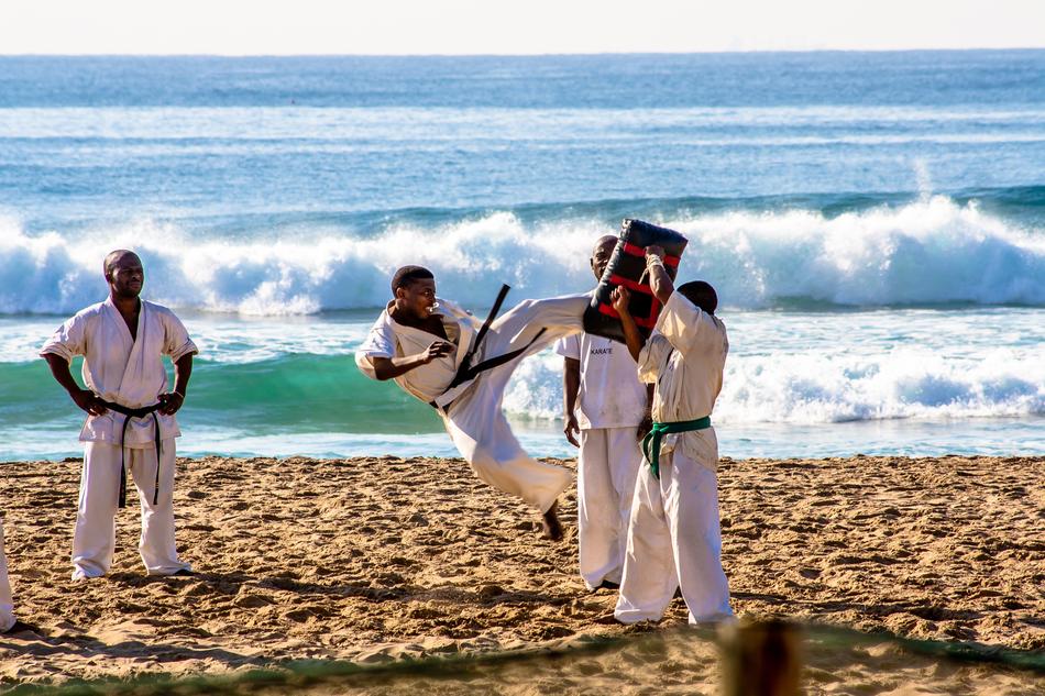 People in kimonos, doing karate on the beautiful, sandy beach near the water with the waves