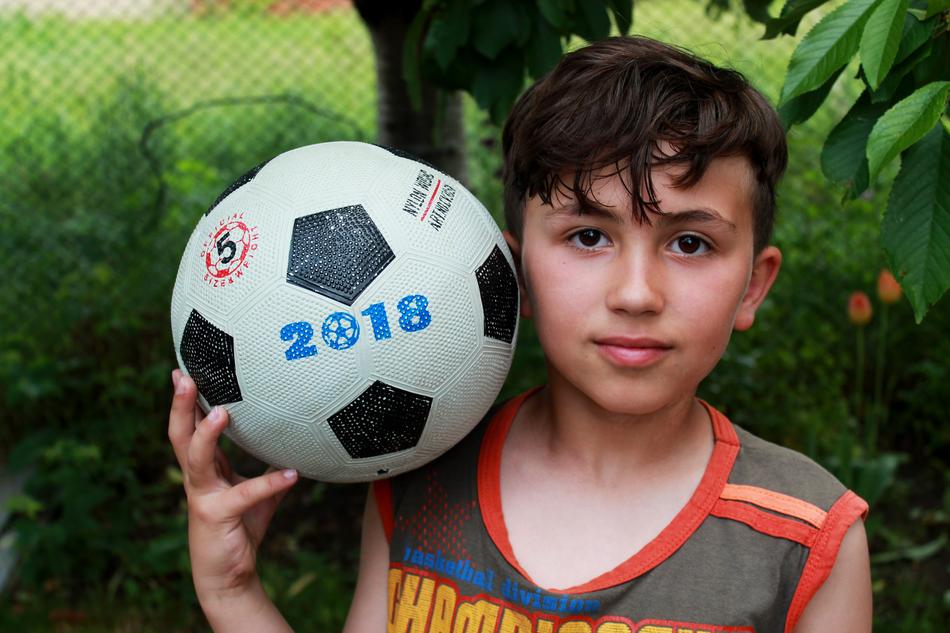 Portrait of a boy child with the colorful football with '2018 sign' among the plants