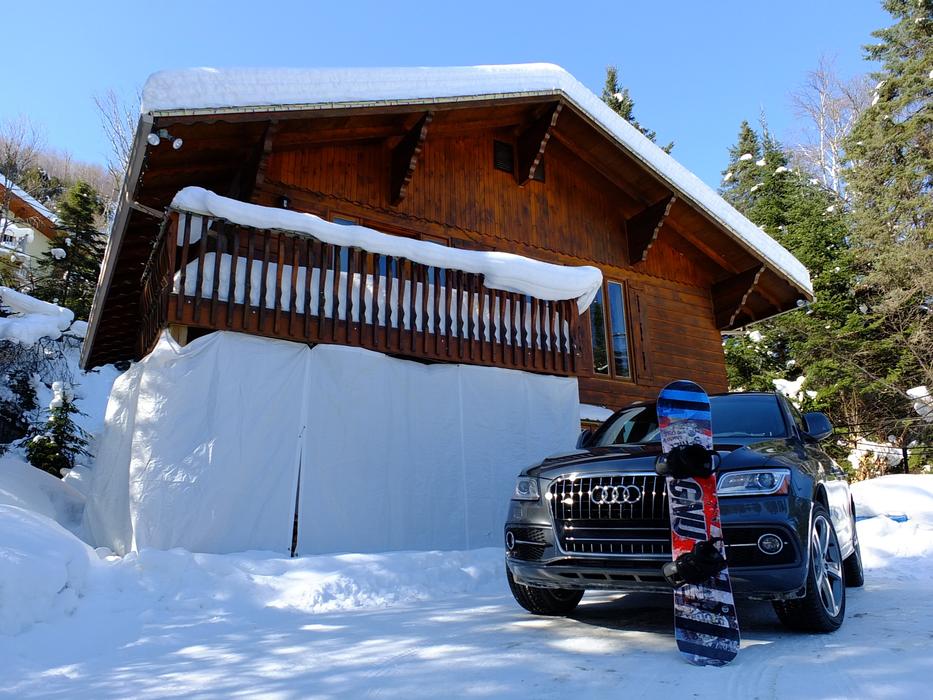 Beautiful, shiny 'Audi' car, with the colorful snowboard, near the beautiful chalet, on the snowy landscape with the trees