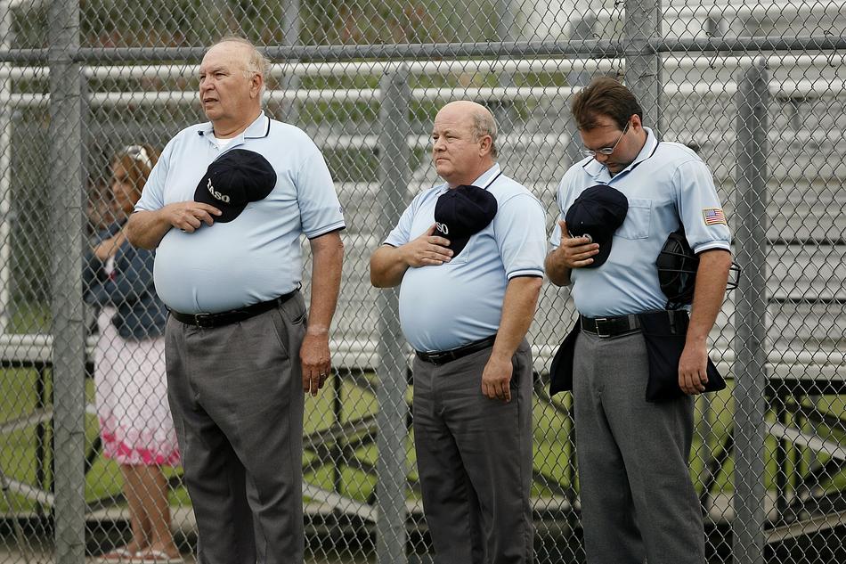 Softball umpires, holding haps at the National Anthem, on the competition in Texas