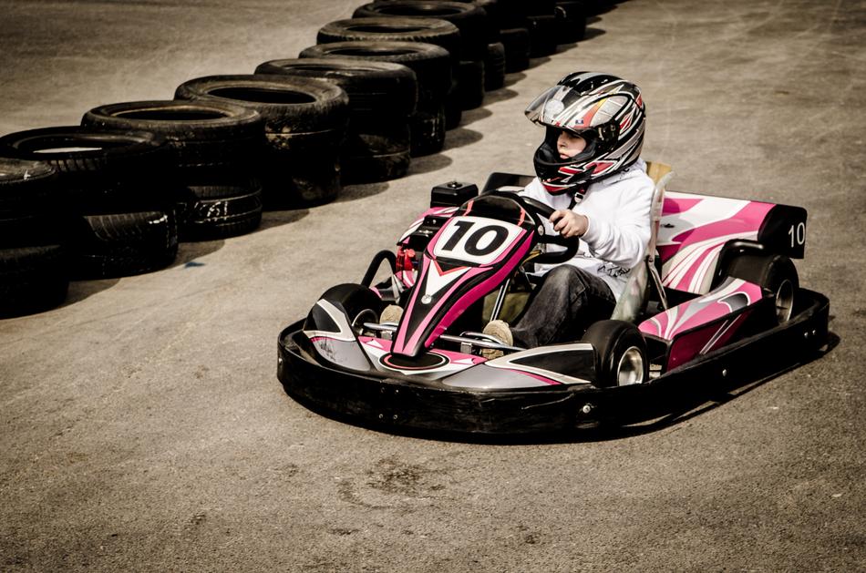 Child in equipment, on the colorful gokart, with number 'ten', near the tyres