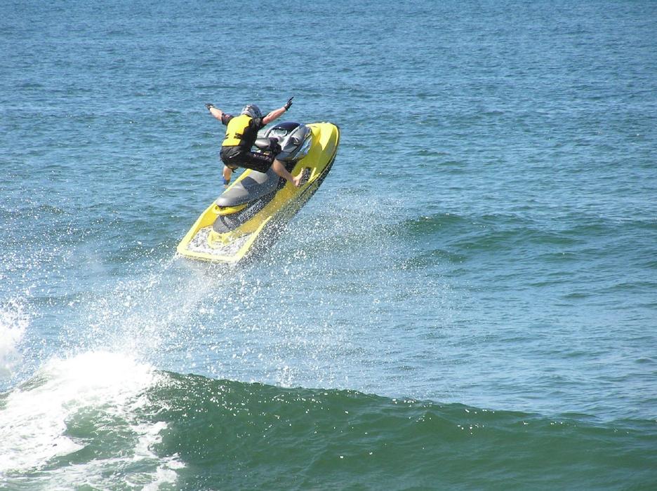 Person on the jetski, in jump, above the green and blue water, with the waves, in light