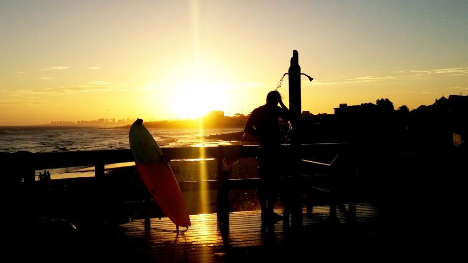 the surfer takes a shower on the ocean against the background of a golden sunset